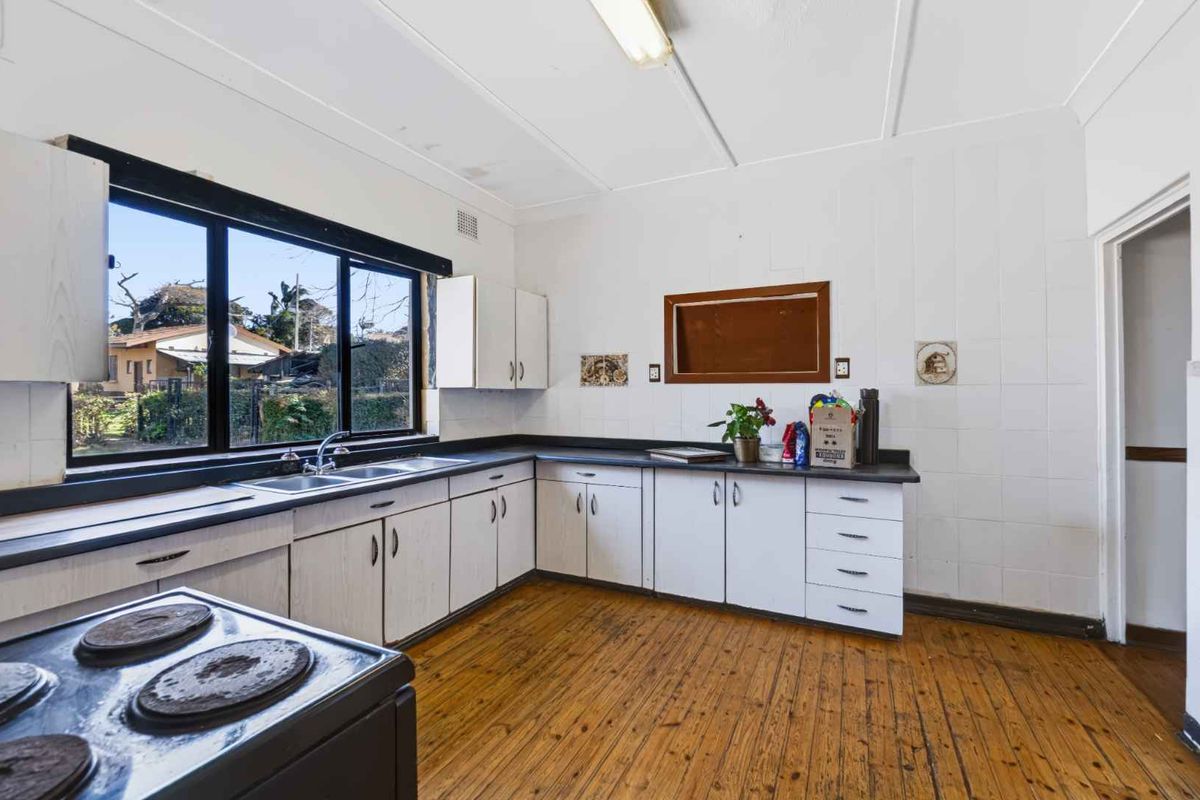 A dated kitchen featuring timber flooring, laminate cabinetry, a double basin sink, and tiled splashbacks, offering significant potential for a modern renovation.