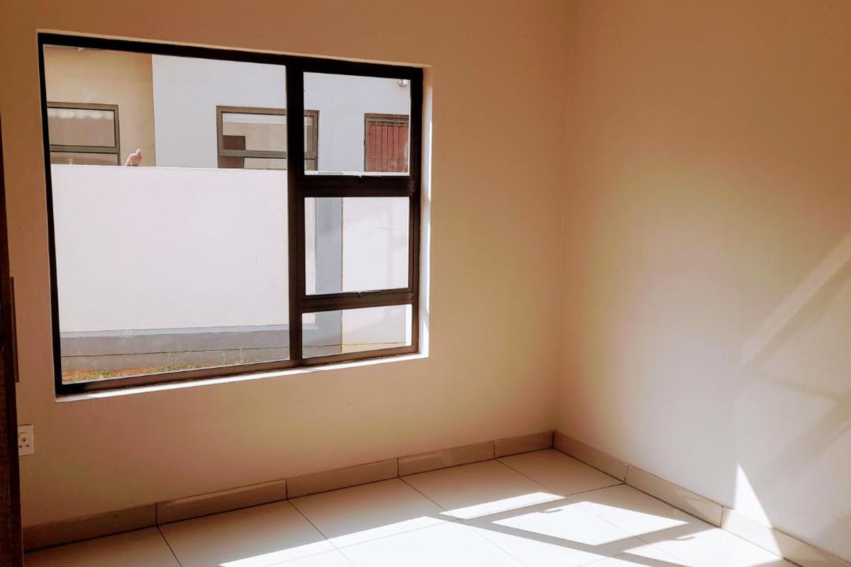 A bright, empty bedroom featuring neutral wall paint, polished floor tiles, and a large window with dark frames.