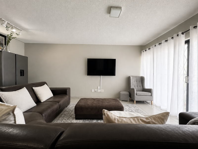 A well-lit living room featuring tiled flooring, a sliding glass door with curtains, and wall-mounted electrical points.