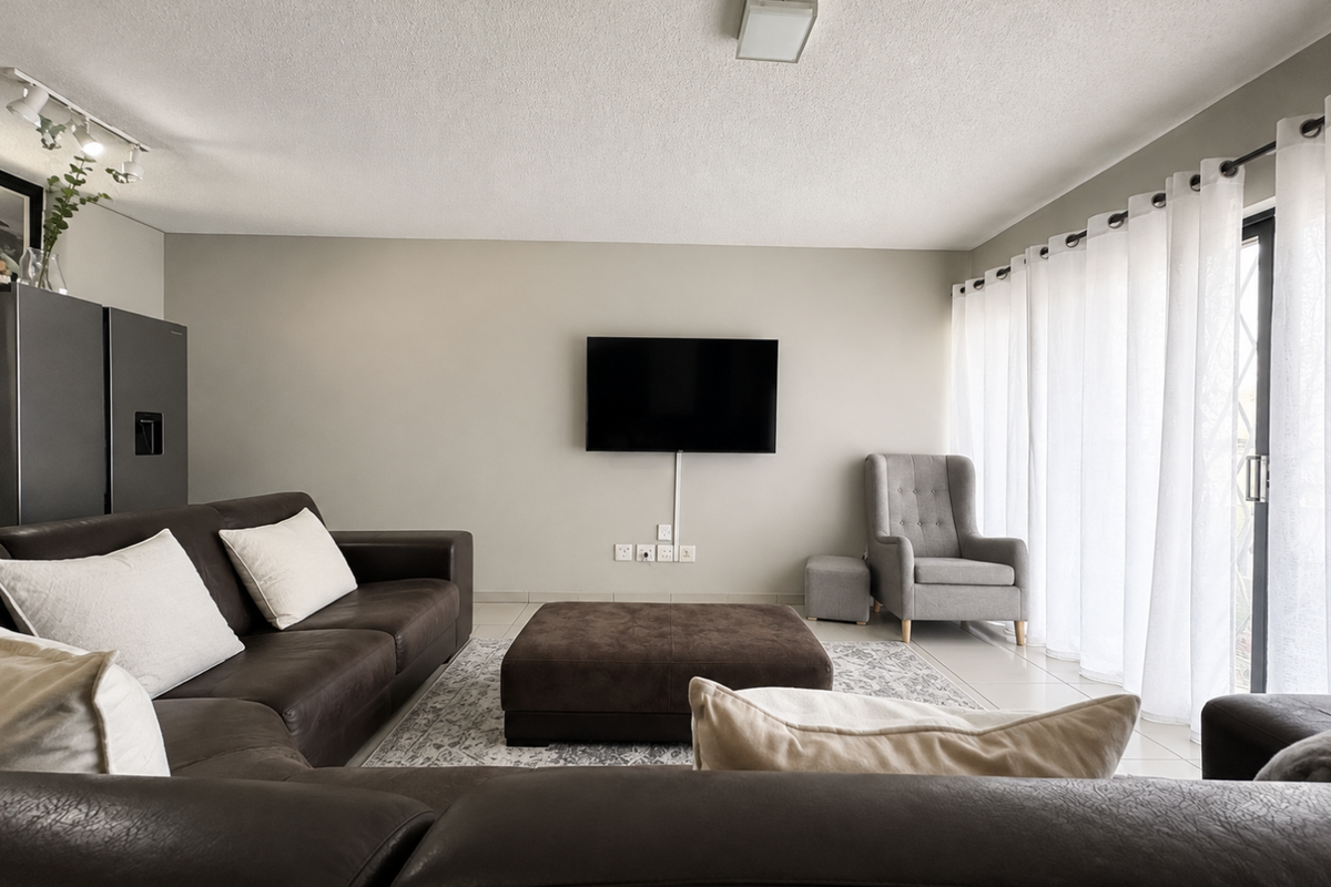 A well-lit living room featuring tiled flooring, a sliding glass door with curtains, and wall-mounted electrical points.