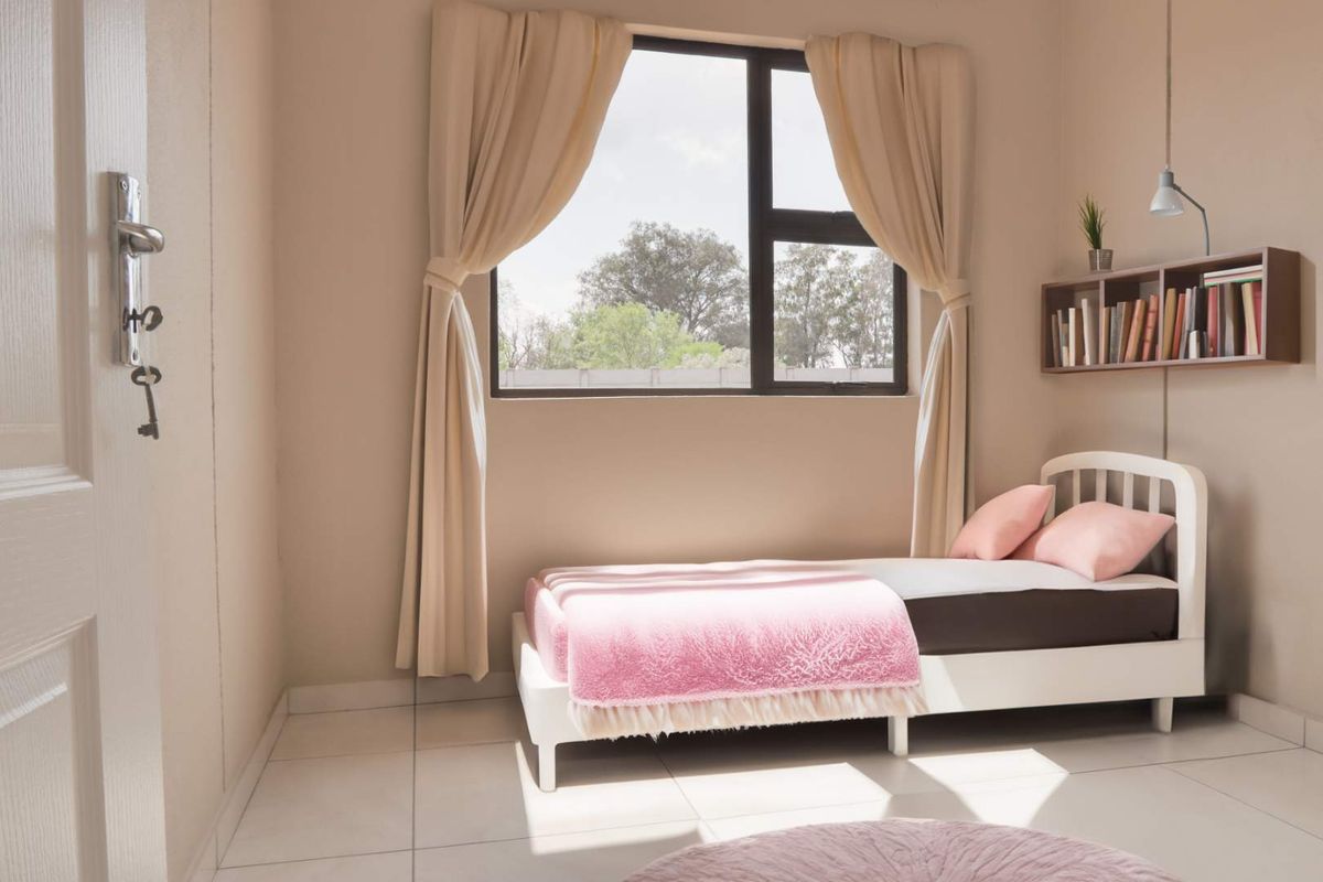 A bright and well-maintained bedroom featuring tiled flooring, neutral wall tones, and a large window providing natural light.