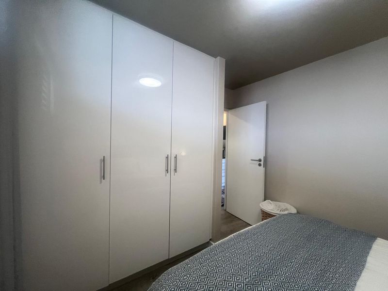 A bedroom featuring a large, modern white built-in wardrobe with sleek handles and neutral wall finishes.
