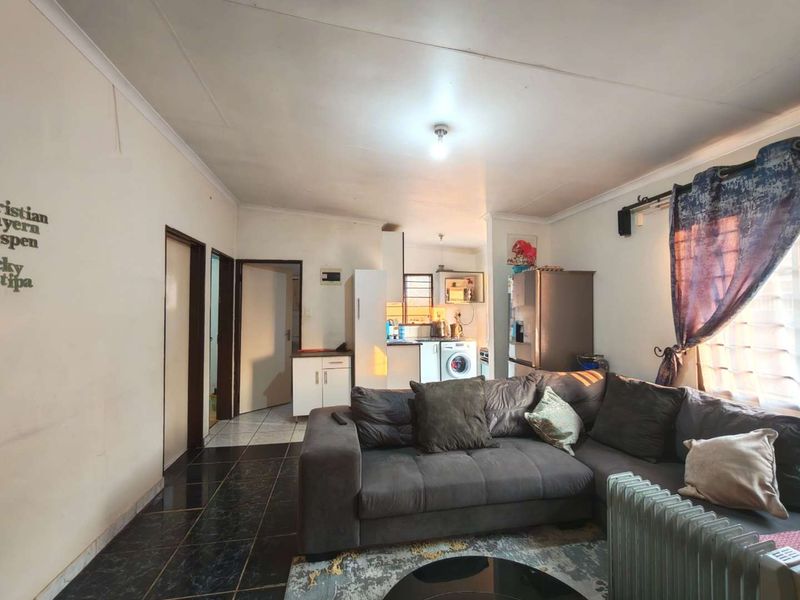 Open-plan living area featuring tiled floors and a compact kitchen space with built-in cabinetry and laundry connections.
