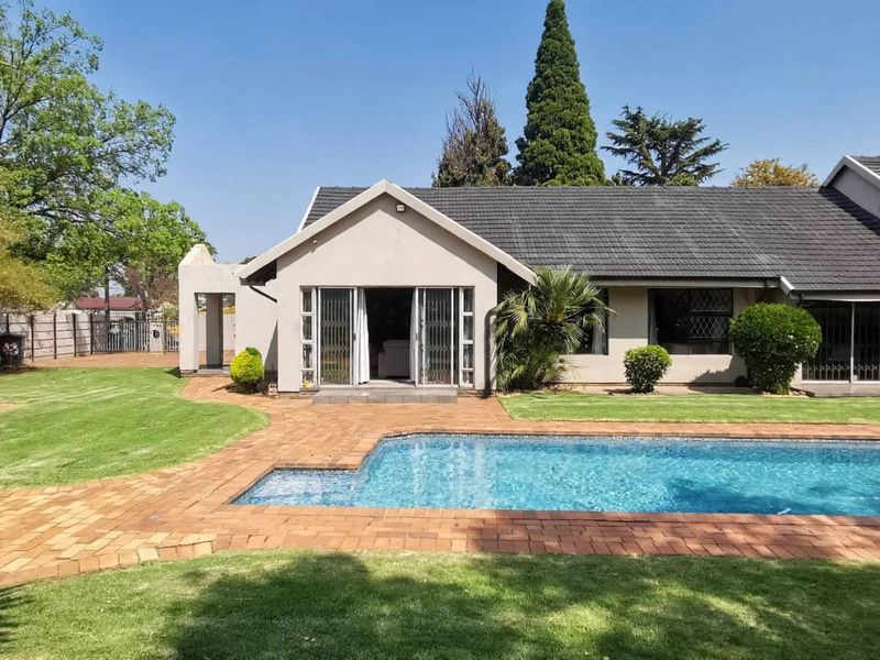 Rear view of the house featuring a swimming pool, brick-paved patio area, and a thatched lapa set within a well-maintained garden.