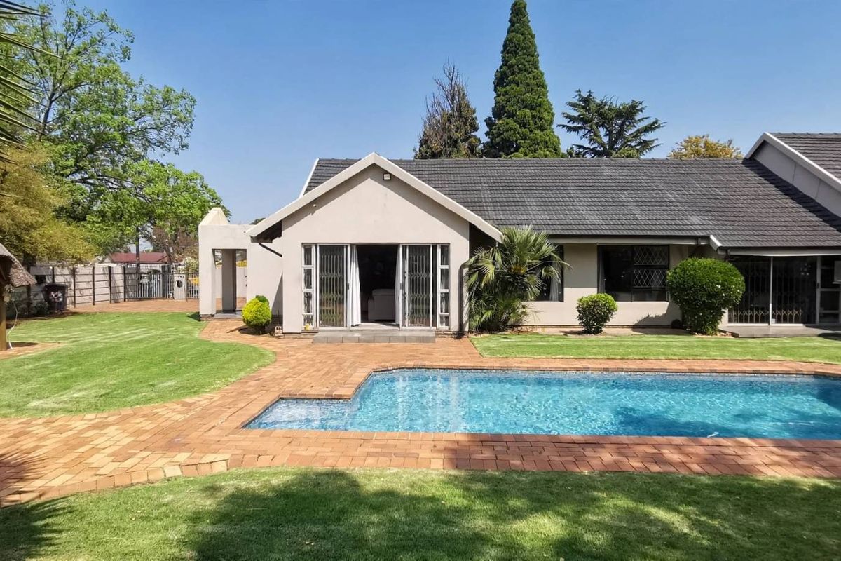 Rear view of the house featuring a swimming pool, brick-paved patio area, and a thatched lapa set within a well-maintained garden.