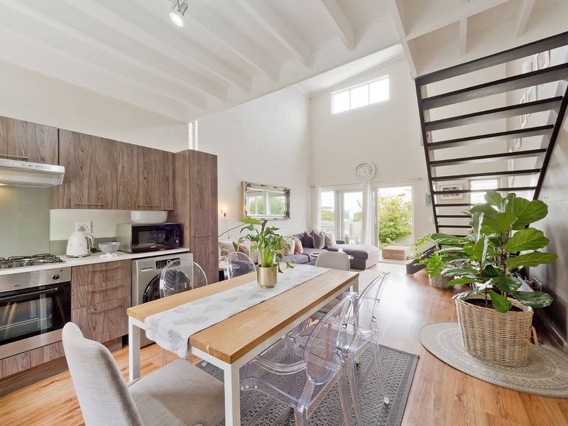 Spacious open-plan living area featuring a modern kitchen with wood-finish cabinetry, high ceilings with exposed beams, and a striking metal staircase leading upstairs.