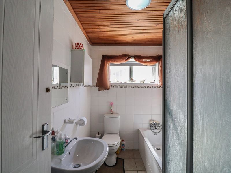 A functional bathroom featuring a pedestal basin, toilet, and bathtub with a shower screen, finished with tiled walls and a timber ceiling.