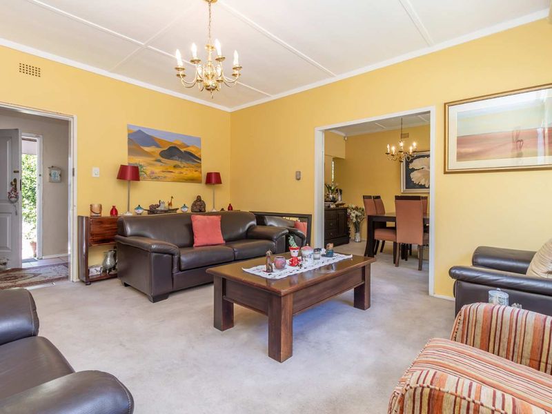 A spacious living room featuring carpeted flooring, a classic chandelier, and an open-plan flow into the adjacent dining area.