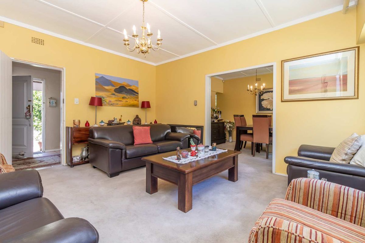 A spacious living room featuring carpeted flooring, a classic chandelier, and an open-plan flow into the adjacent dining area.