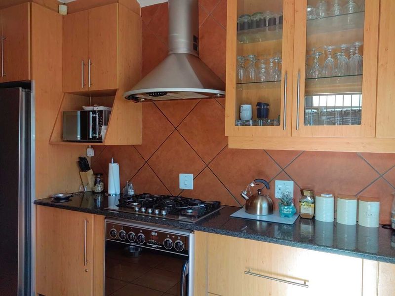 A functional kitchen featuring light wood cabinetry, granite countertops, a gas hob with extractor fan, and a tiled backsplash.