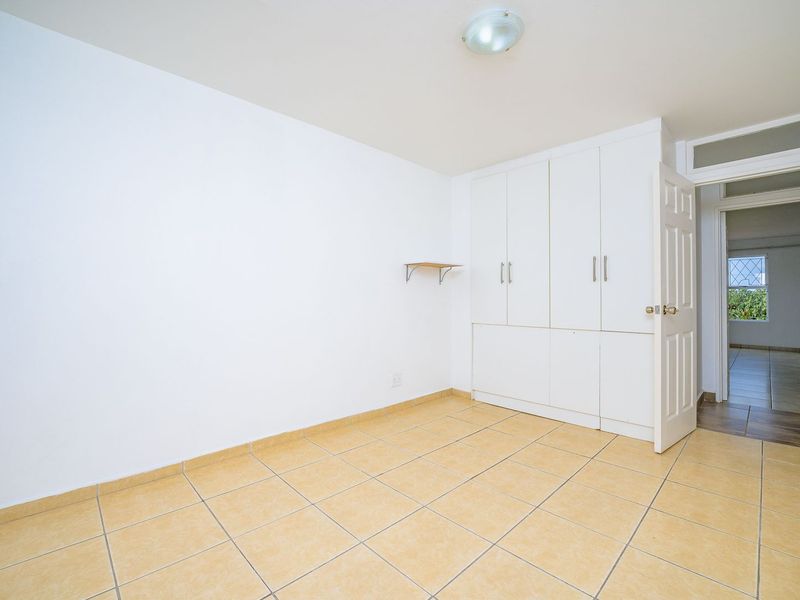 A bright, empty bedroom featuring neutral tiled flooring and ample built-in cupboard storage, offering a clean canvas for personalization.