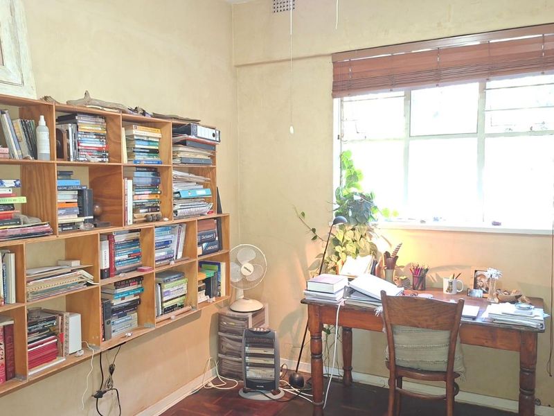 A functional home office featuring built-in wooden shelving, classic timber parquet flooring, and a window with fitted blinds, offering a practical workspace.