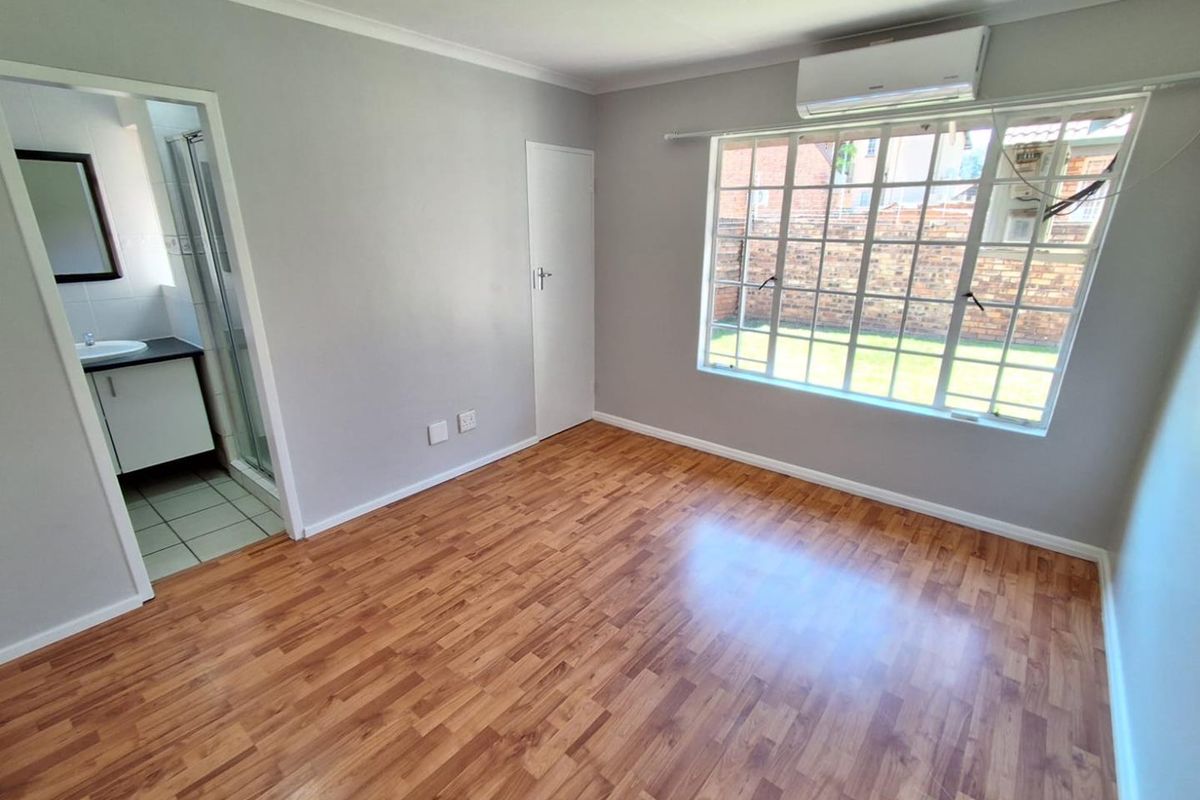 A bright, empty bedroom featuring laminate flooring, an air conditioning unit, and an en-suite bathroom with a shower.