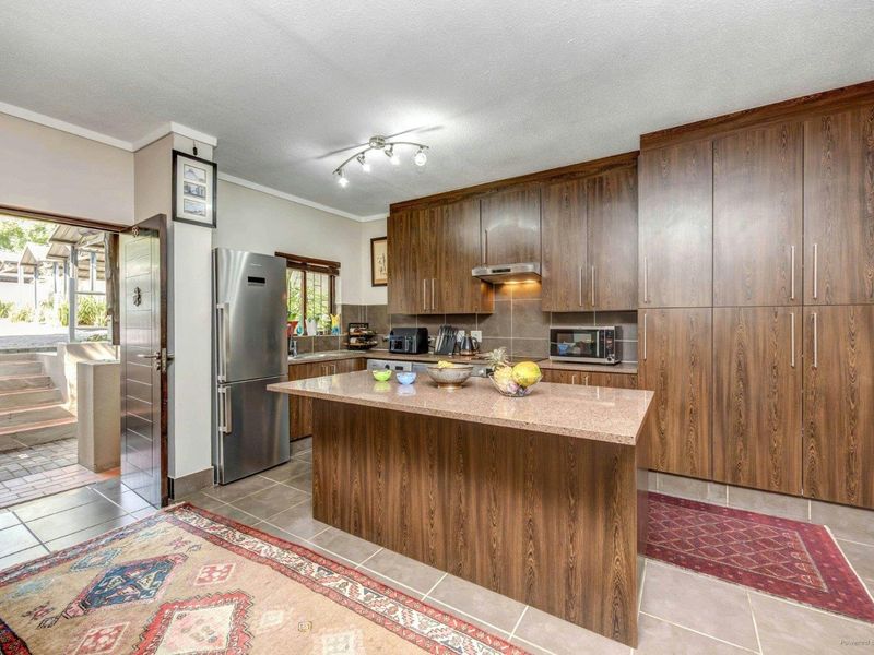 A well-maintained kitchen featuring dark wood cabinetry, granite countertops, a central island, and tiled flooring, with direct access to an outdoor patio area.