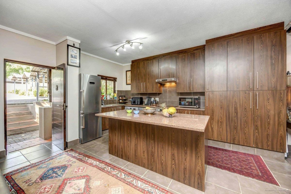 A well-maintained kitchen featuring dark wood cabinetry, granite countertops, a central island, and tiled flooring, with direct access to an outdoor patio area.