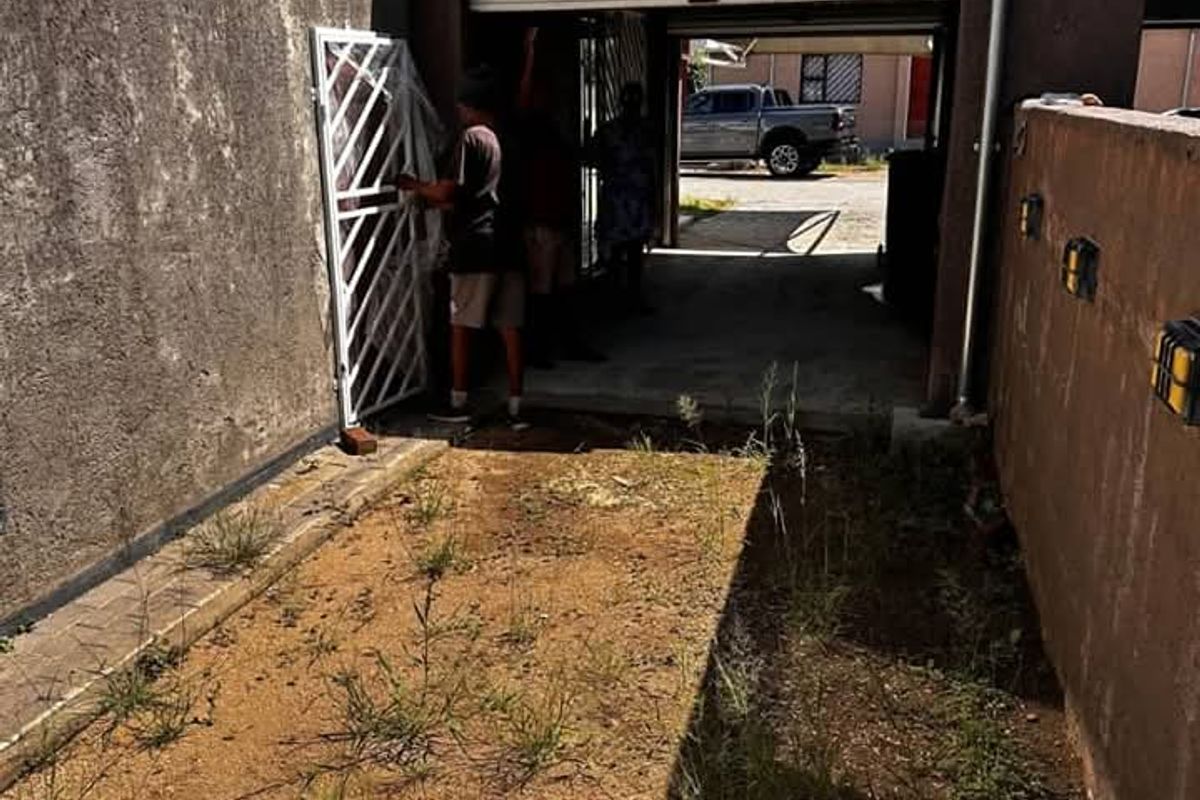Rear exterior view of the townhouse featuring a small yard area, concrete walling, and access to the garage space.