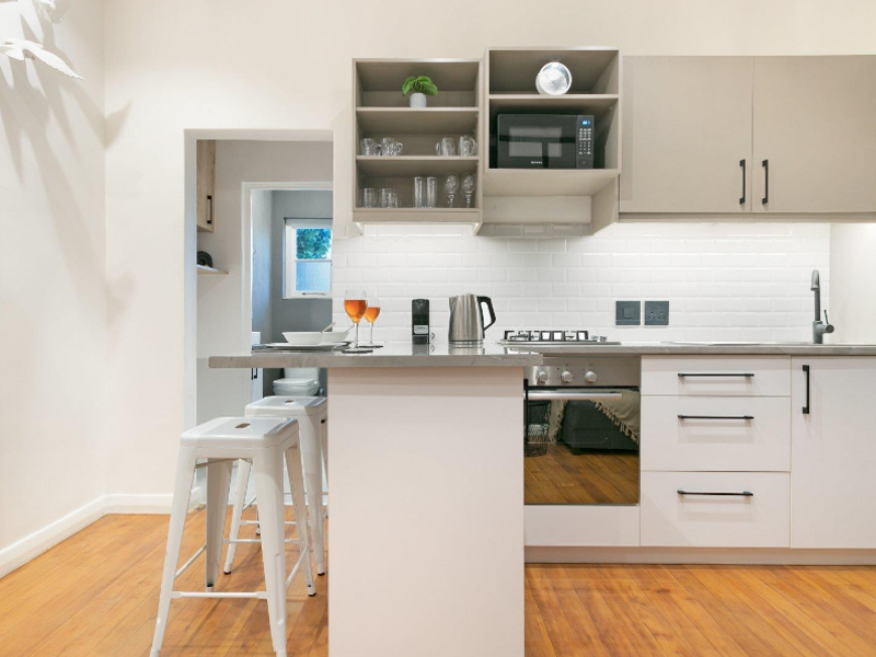 Modern kitchen featuring sleek cabinetry, subway tile backsplash, gas hob, built-in oven, and stone countertops, complemented by warm hardwood flooring.