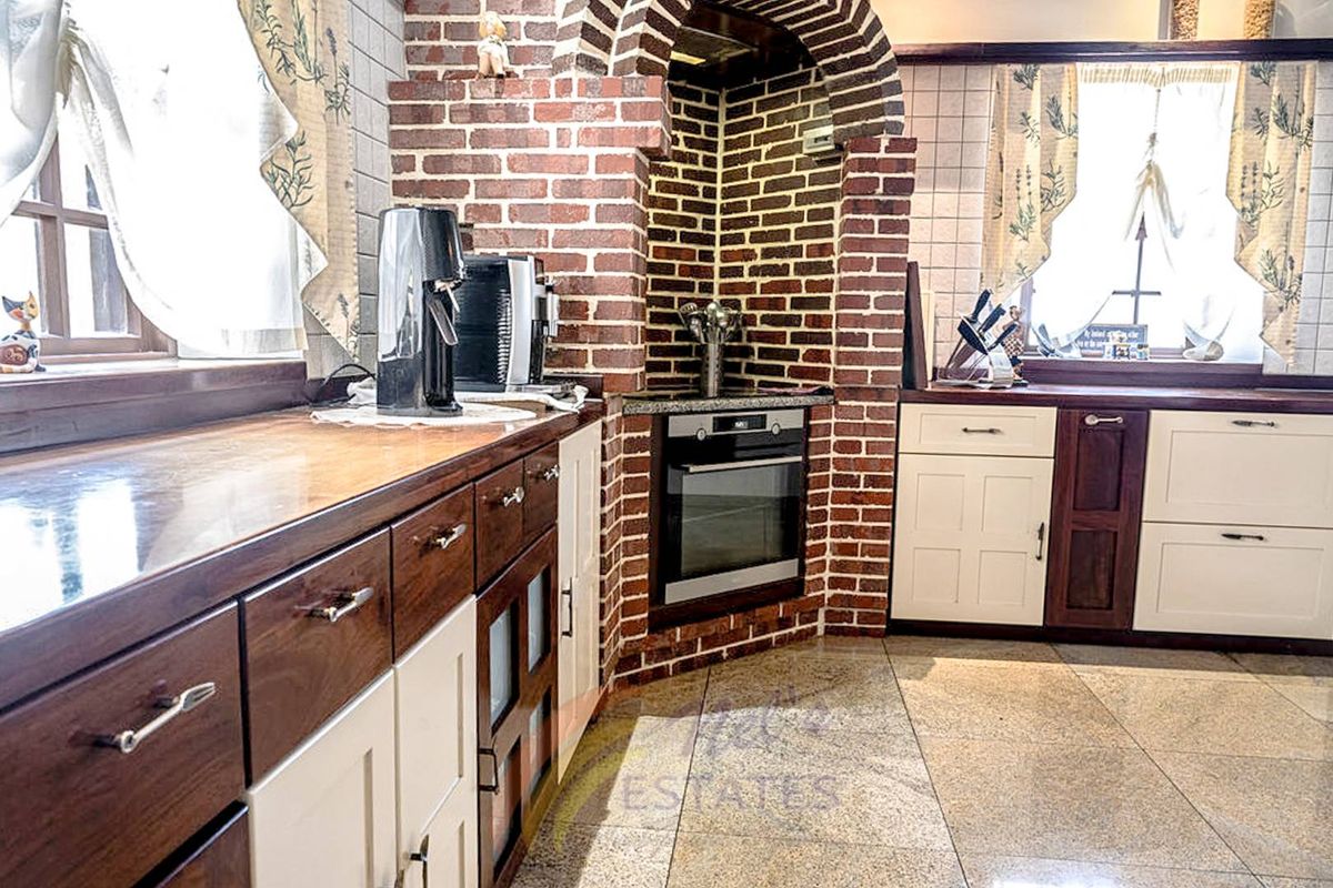 A rustic-style kitchen featuring a brick-encased built-in oven, stone tile flooring, and a mix of white and dark wood cabinetry.