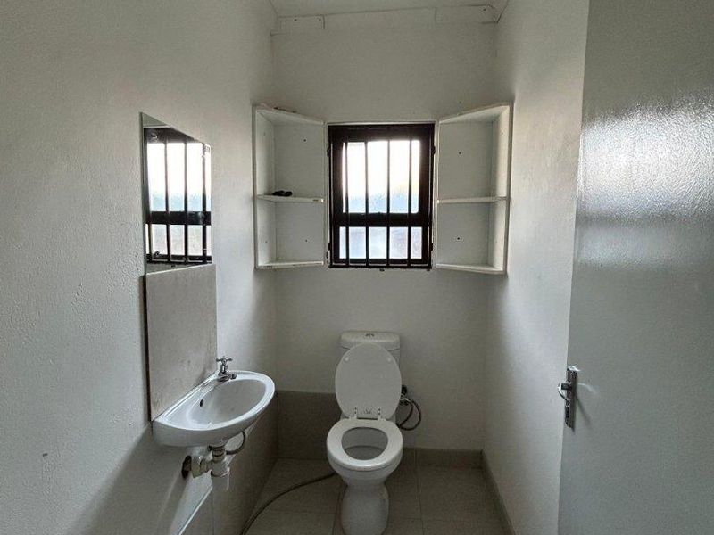 A compact bathroom featuring a wall-mounted basin, toilet, tiled flooring, and built-in shelving, with security bars fitted to the window.