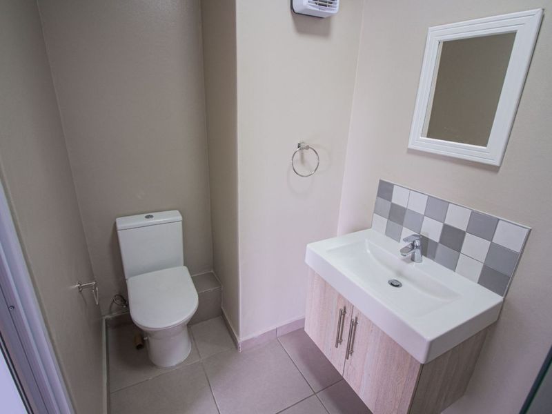 A clean and modern bathroom featuring a vanity cabinet with basin, tiled splashback, and a standard toilet.