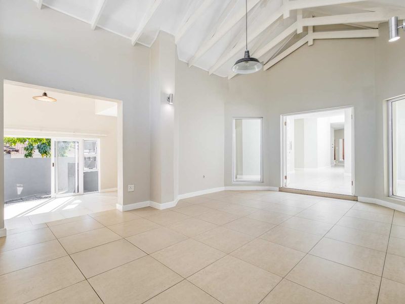 Spacious, light-filled living area featuring high vaulted ceilings with exposed rafters, neutral tiled flooring, and seamless access to adjacent spaces through large openings.