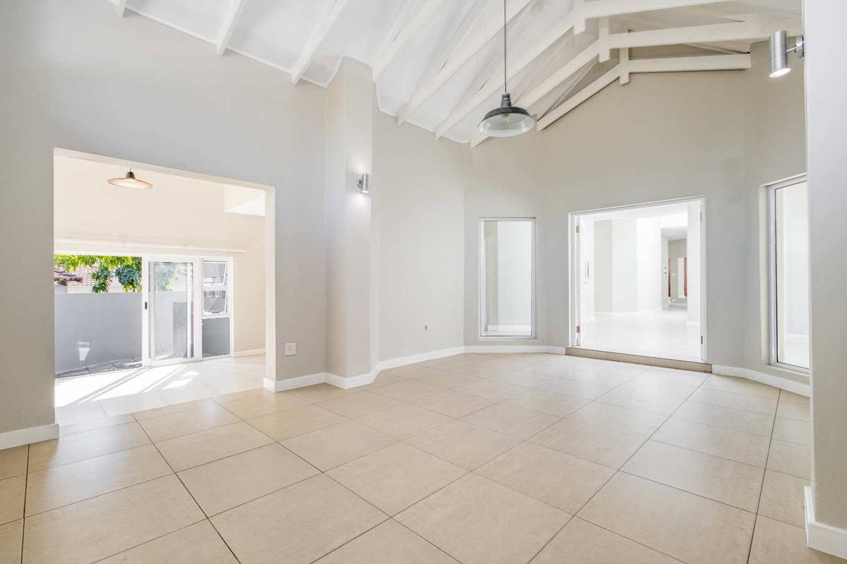 Spacious, light-filled living area featuring high vaulted ceilings with exposed rafters, neutral tiled flooring, and seamless access to adjacent spaces through large openings.