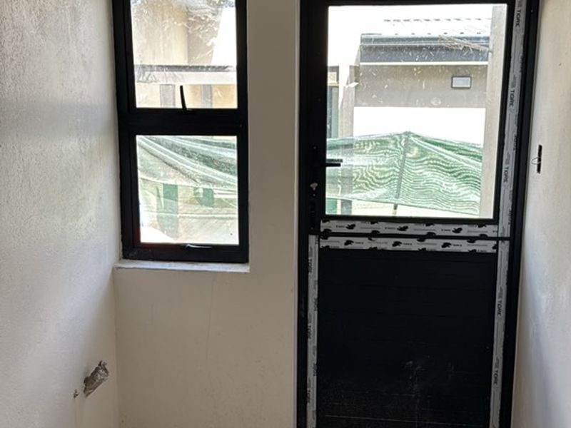A small, unfinished utility space featuring tiled flooring, an aluminium door, and a window, currently awaiting final finishes and trim work.