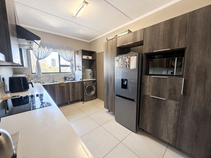 Modern kitchen featuring dark wood-grain cabinetry, integrated appliances, electric hob, extractor fan, and tiled flooring with a dedicated laundry area.