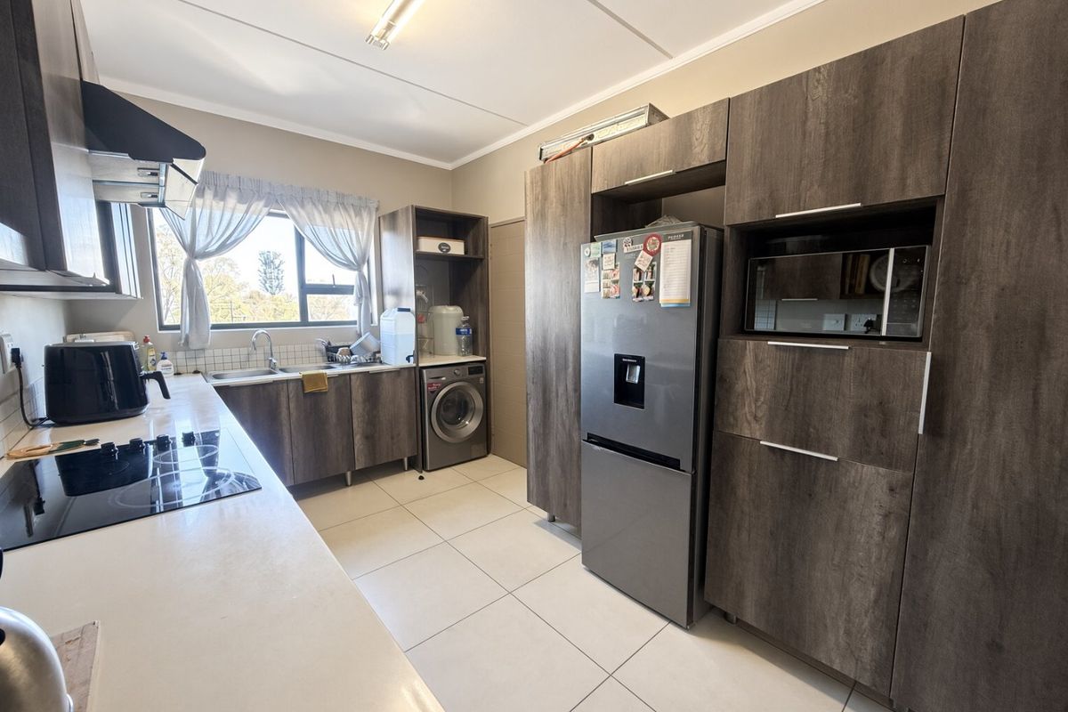 Modern kitchen featuring dark wood-grain cabinetry, integrated appliances, electric hob, extractor fan, and tiled flooring with a dedicated laundry area.