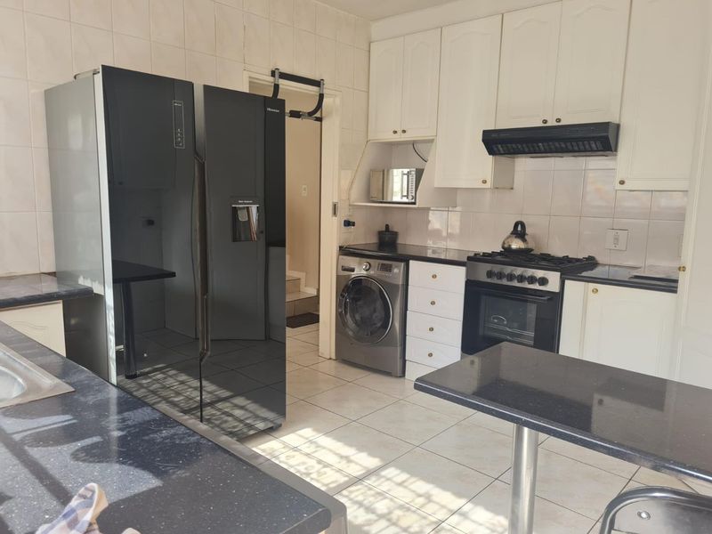 Functional kitchen featuring white cabinetry, dark granite countertops, gas stove with extractor fan, and tiled finishes throughout.