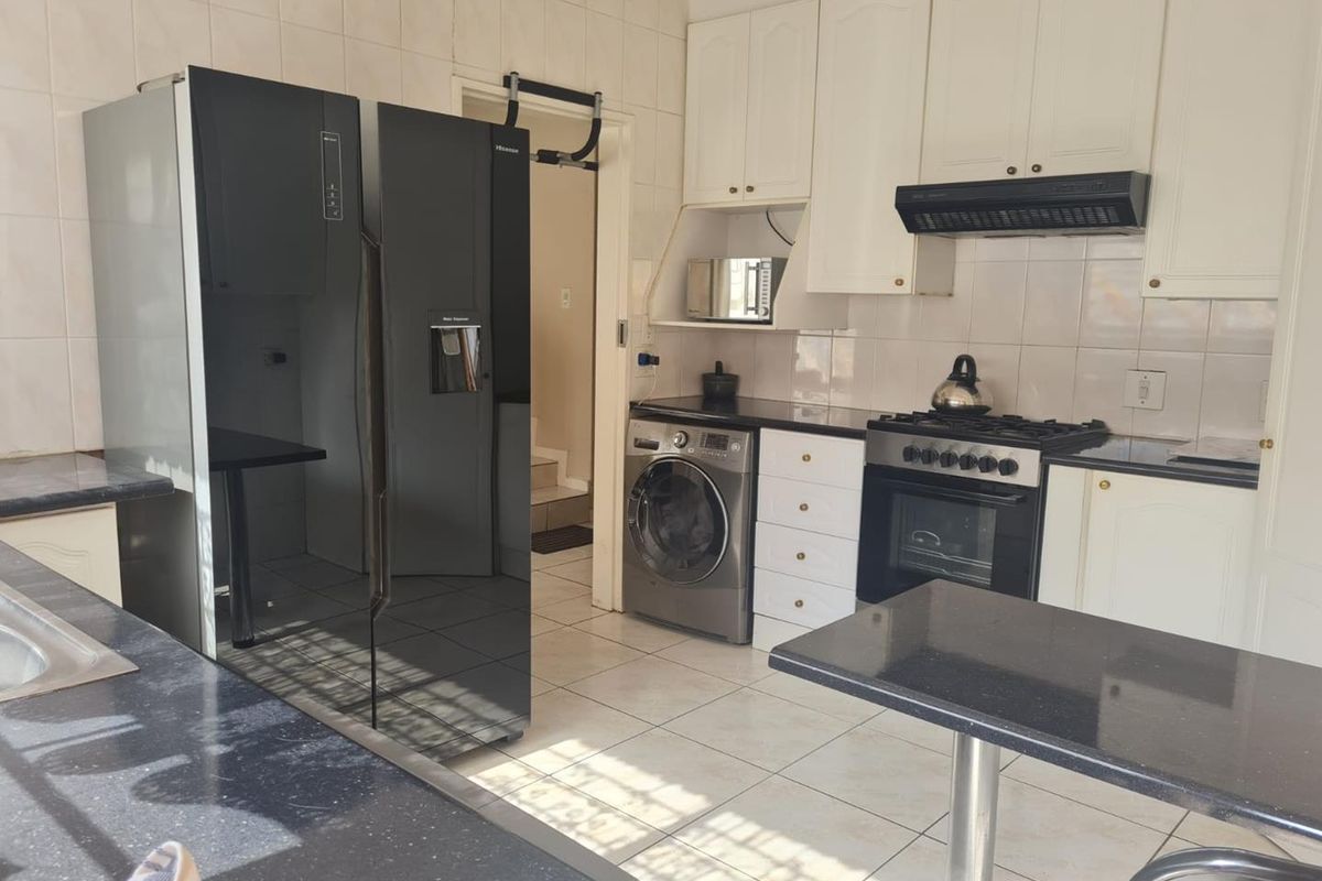Functional kitchen featuring white cabinetry, dark granite countertops, gas stove with extractor fan, and tiled finishes throughout.