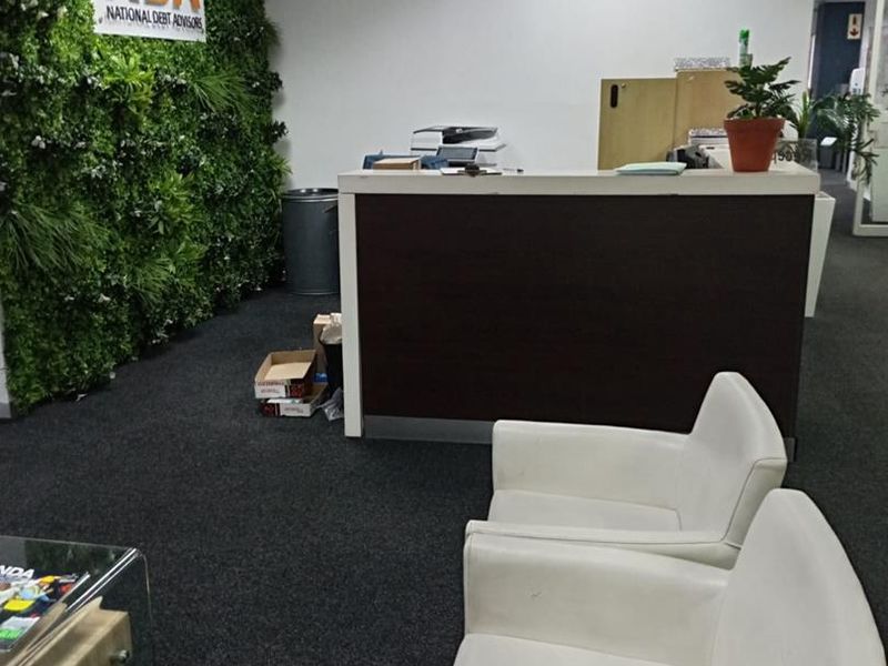 Office reception area featuring a dark reception desk, carpeted flooring, and a decorative green feature wall with corporate branding.