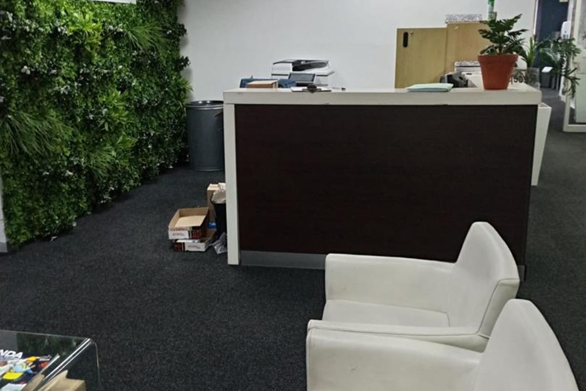 Office reception area featuring a dark reception desk, carpeted flooring, and a decorative green feature wall with corporate branding.