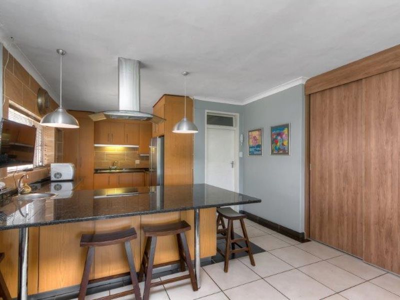 Open-plan kitchen featuring a granite island, built-in wooden cabinetry, stainless steel extractor fan, and tiled flooring with integrated storage.