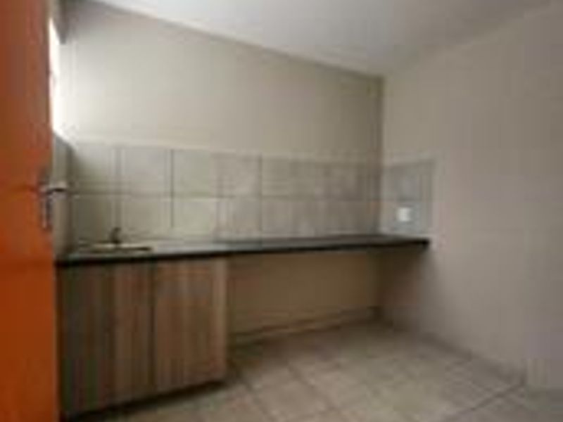 A functional, empty kitchen area featuring built-in cabinetry, a tiled splashback, and tiled flooring, providing a clean slate for customization.