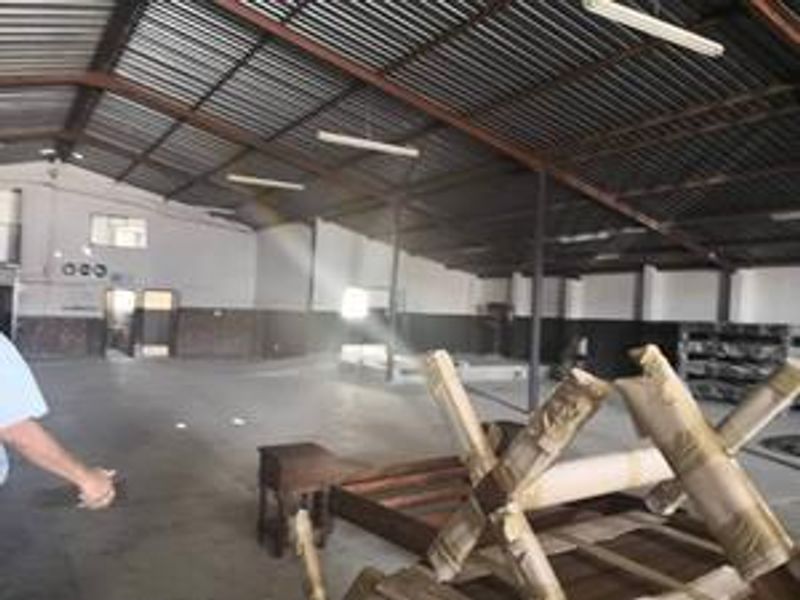 Spacious industrial utility area featuring high exposed steel roof trusses, corrugated metal roofing, and durable concrete flooring, suitable for various commercial or storage uses.