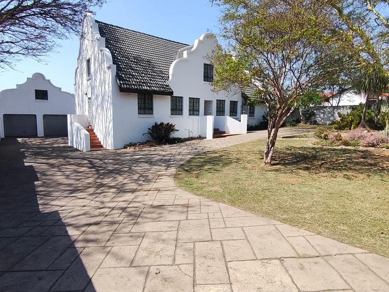 A well-maintained Cape Dutch style house featuring a paved driveway, double garage, and established garden.