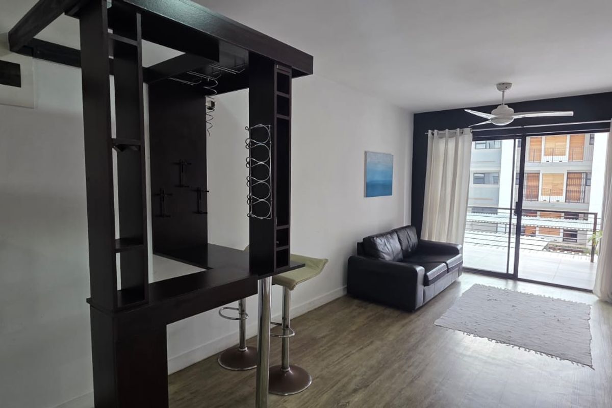 Open-plan living area featuring laminate flooring, a ceiling fan, and a built-in bar unit, with direct access to a balcony through sliding glass doors.