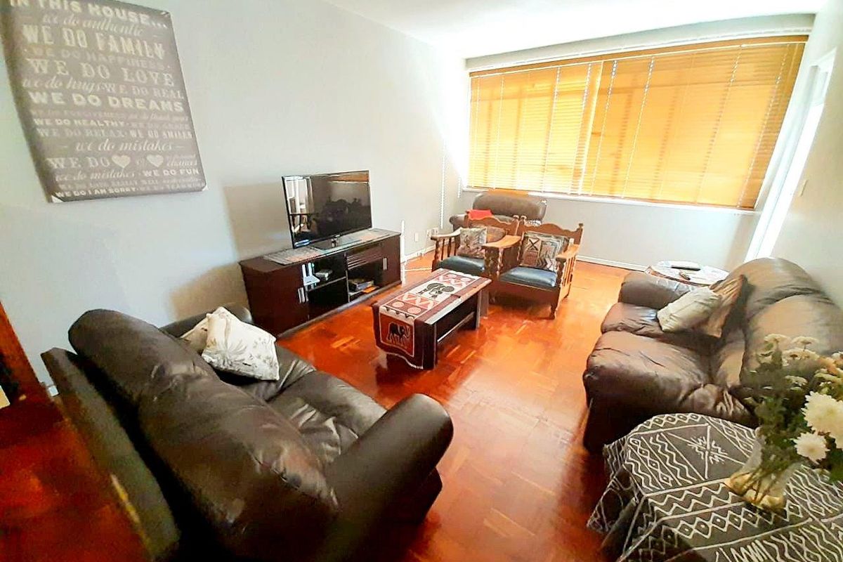 A spacious living room featuring polished hardwood flooring and large windows with fitted wooden blinds, providing ample natural light.
