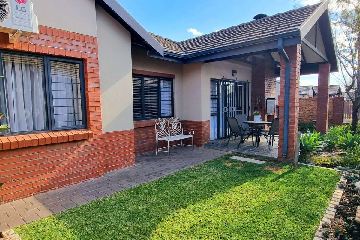 A well-maintained rear exterior featuring a covered patio with a built-in braai, brick facade, paved walkway, and a neat garden area.
