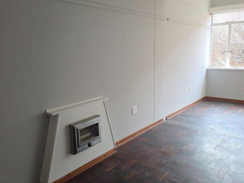 An empty living room featuring original parquet flooring and a built-in gas heater, offering a blank canvas for renovation.