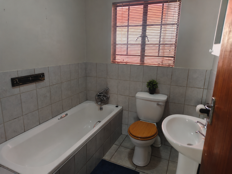A functional bathroom featuring a standard bathtub, pedestal basin, and toilet with neutral wall and floor tiling.