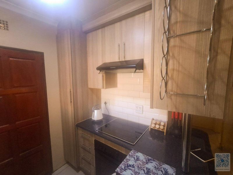 A compact kitchen featuring modern light wood cabinetry, a dark countertop, subway tile backsplash, and a built-in electric hob with an extractor fan.