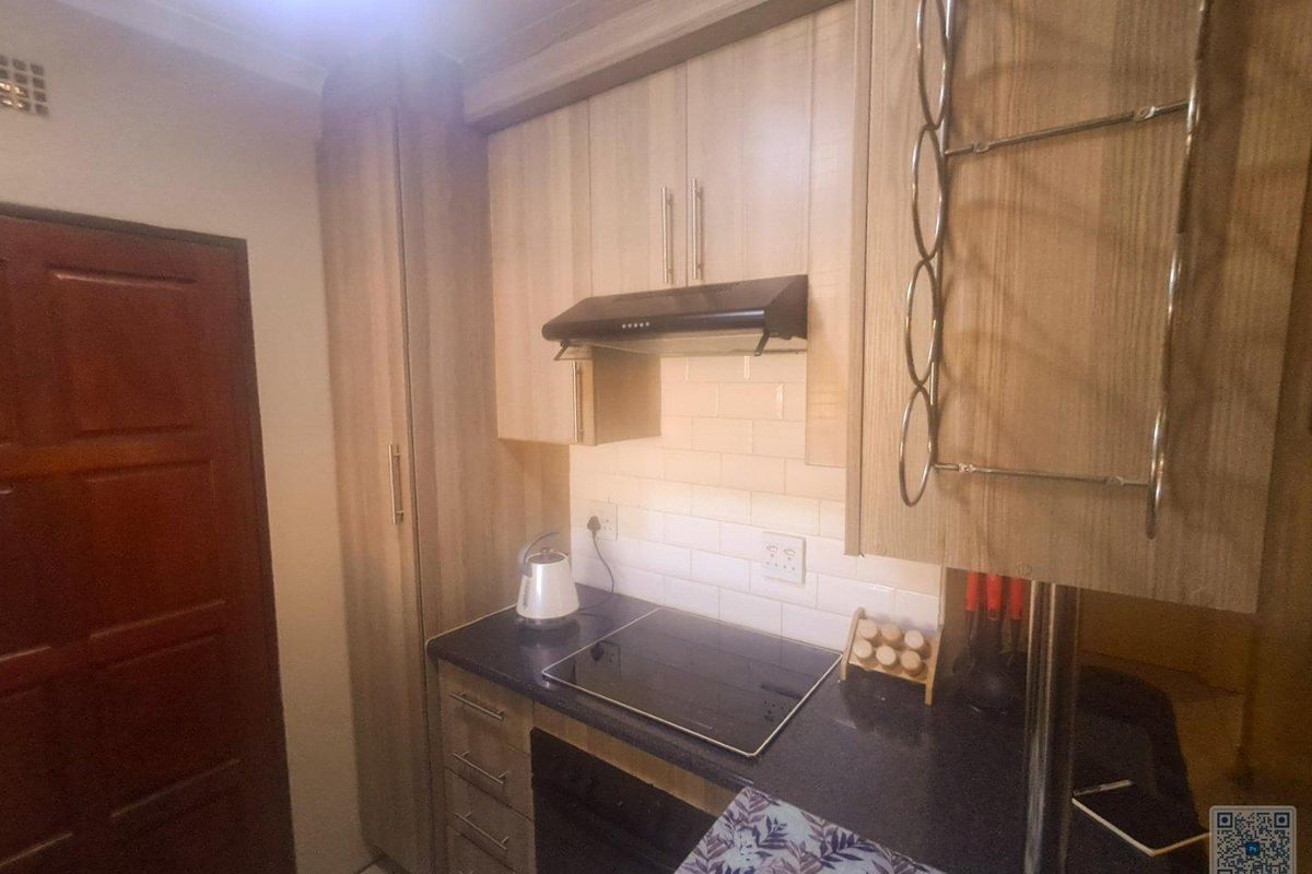 A compact kitchen featuring modern light wood cabinetry, a dark countertop, subway tile backsplash, and a built-in electric hob with an extractor fan.