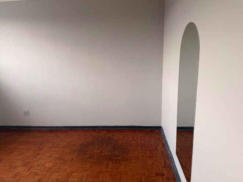 An empty bedroom featuring traditional parquet flooring, neutral walls, and a built-in arched wall mirror.