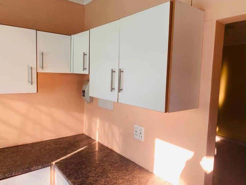A compact kitchen area featuring white wall-mounted cabinetry and dark laminate countertops, requiring minor cosmetic updates to improve the overall aesthetic.