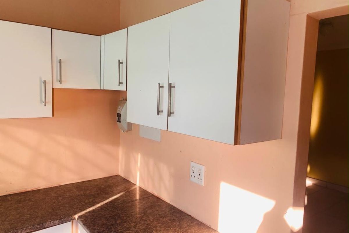 A compact kitchen area featuring white wall-mounted cabinetry and dark laminate countertops, requiring minor cosmetic updates to improve the overall aesthetic.