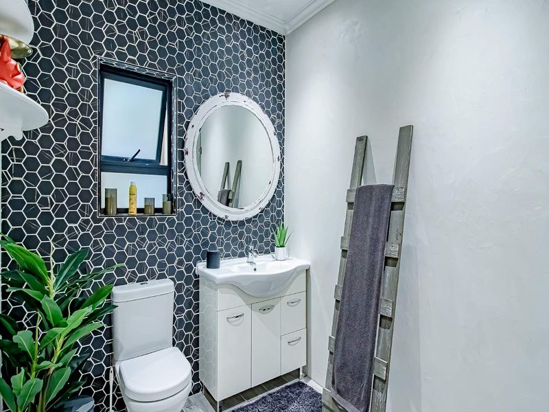 A modern bathroom featuring a striking black hexagonal tiled feature wall, a white vanity with integrated basin, and a contemporary toilet.