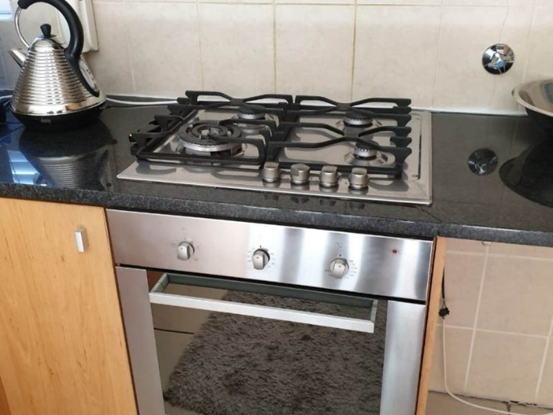 A functional kitchen area featuring a stainless steel gas hob, built-in oven, granite countertops, and neutral tiled backsplash.