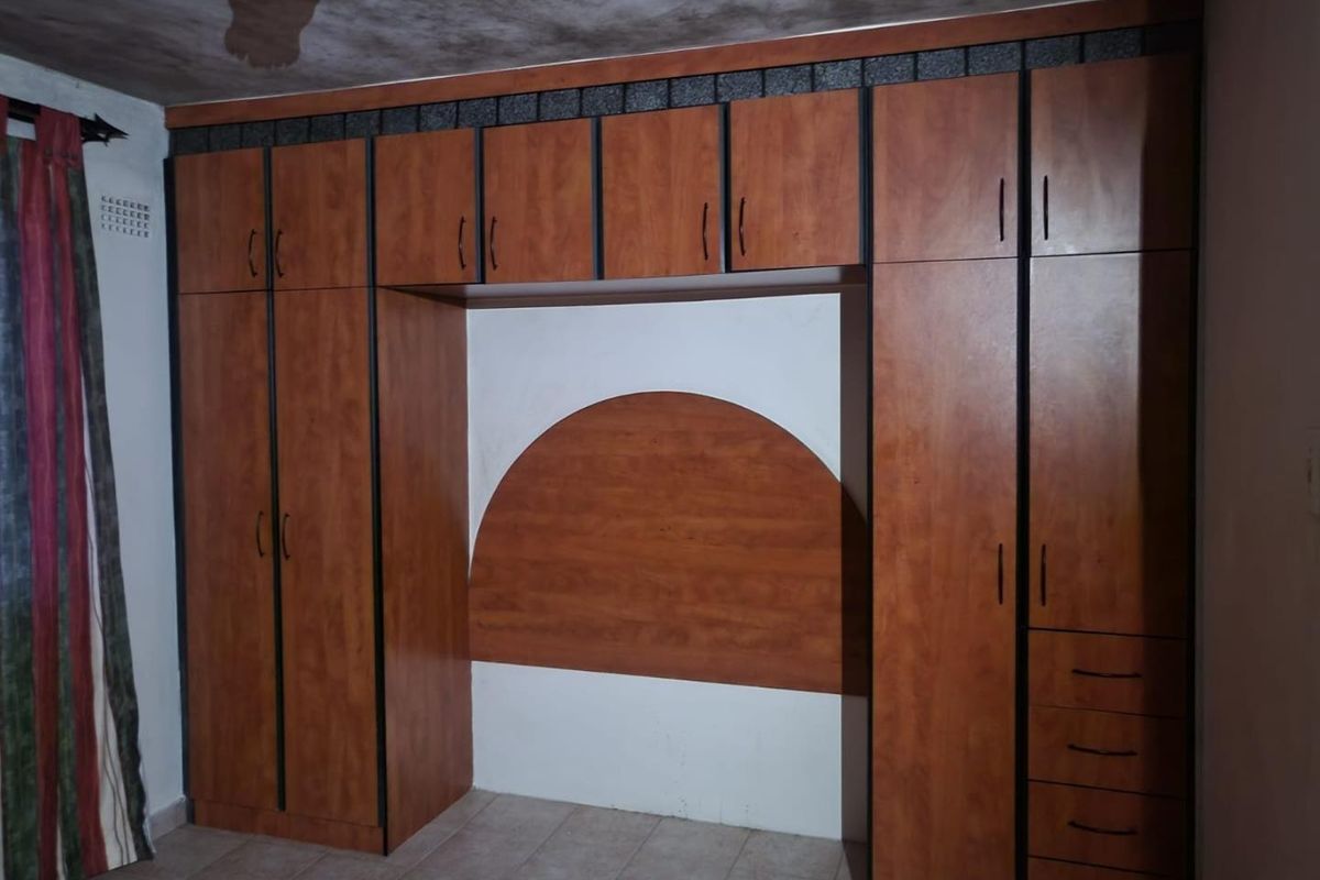Bedroom featuring extensive built-in wooden cabinetry with an integrated headboard and tiled flooring. The ceiling shows signs of water damage.